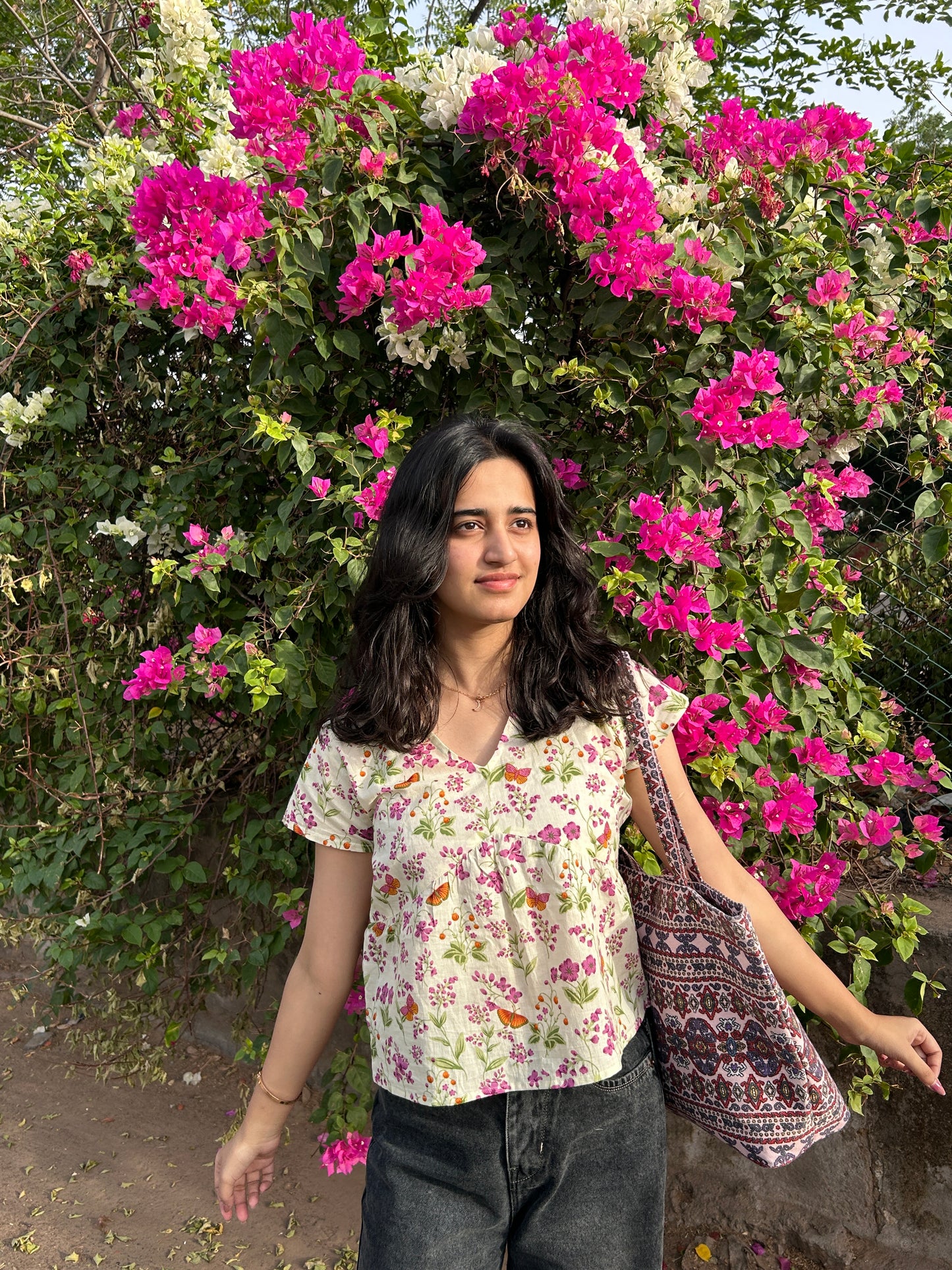 Woman in floral cotton short sleeve top with bird print standing in front of bougainvillea