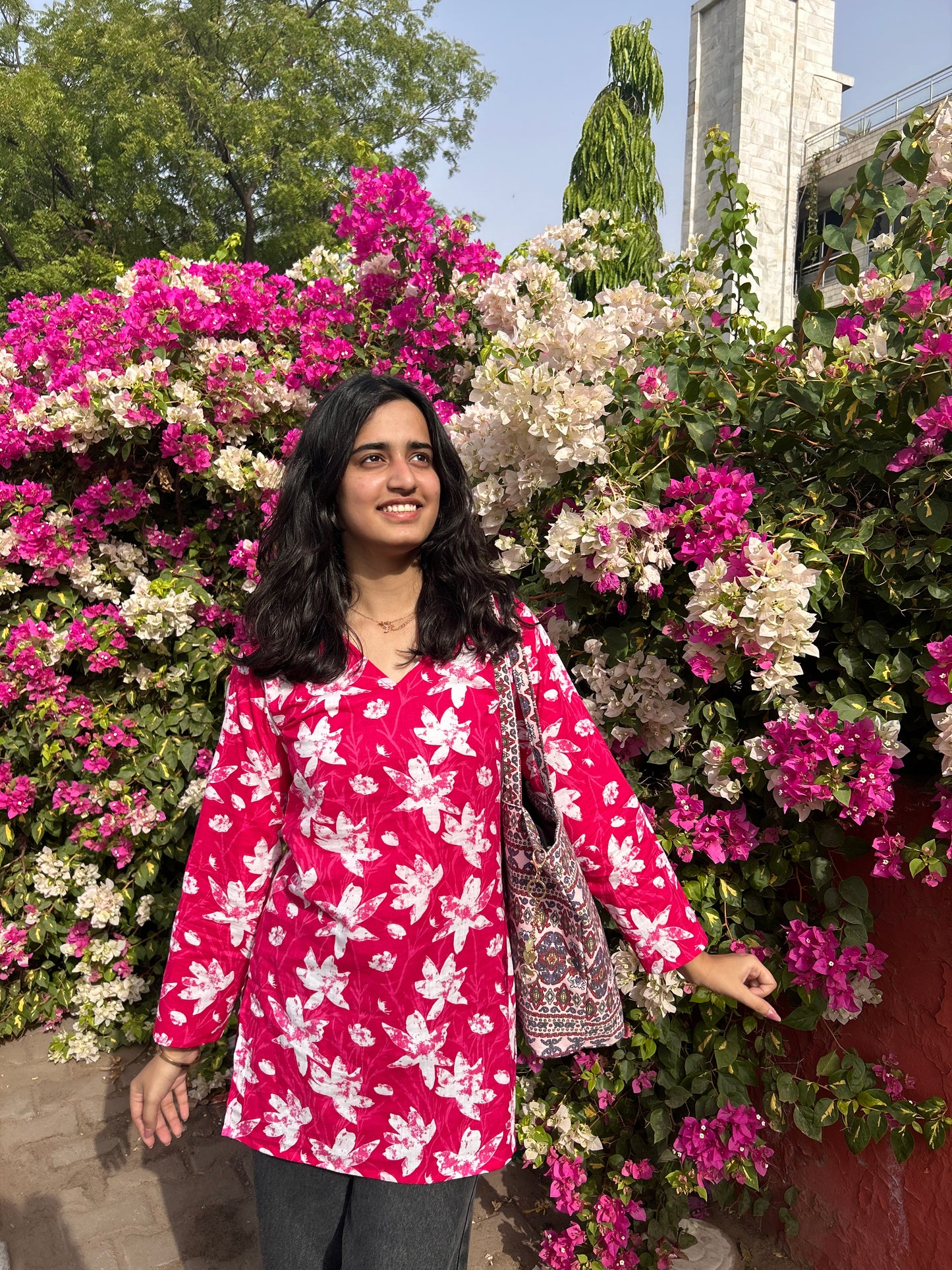 Woman wearing pink floral cotton short kurta in front of pink and white bougainvillea